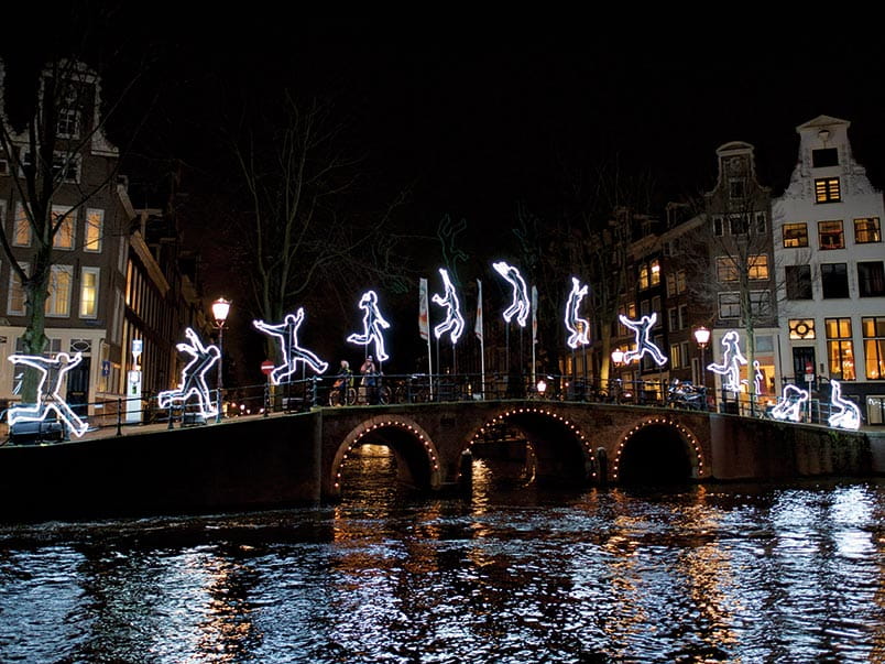 A light installations of a person jumping over a canal bridge in Amsterdam at night A light installations of a person jumping over a canal bridge in Amsterdam at night